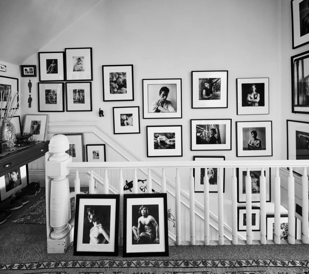 Top of the entrance stairway where black-and-white photographs of male nudes and portraits hang in a salon-style.
